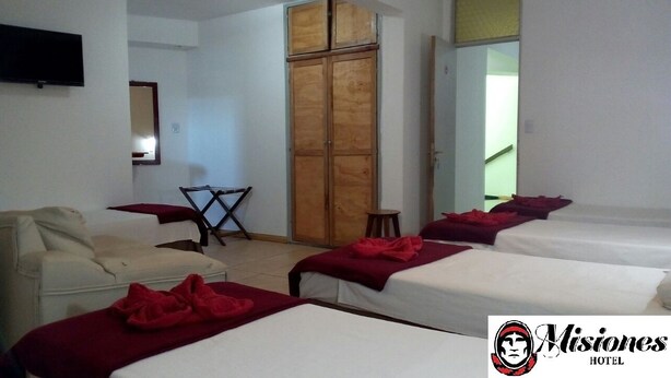 A hotel room with two beds, a sofa, a TV, a wooden wardrobe, and a small table.