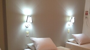 A hotel room with two beds, each with white bedding and a red throw blanket. There are wall-mounted lights above each bed.