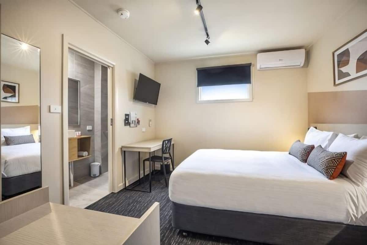 A hotel room with a bed, a desk, a chair, a TV, and a mirror.
