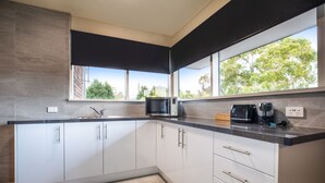 Une cuisine moderne avec des meubles blancs, un plan de travail noir, un four à micro-ondes et une machine à café.
