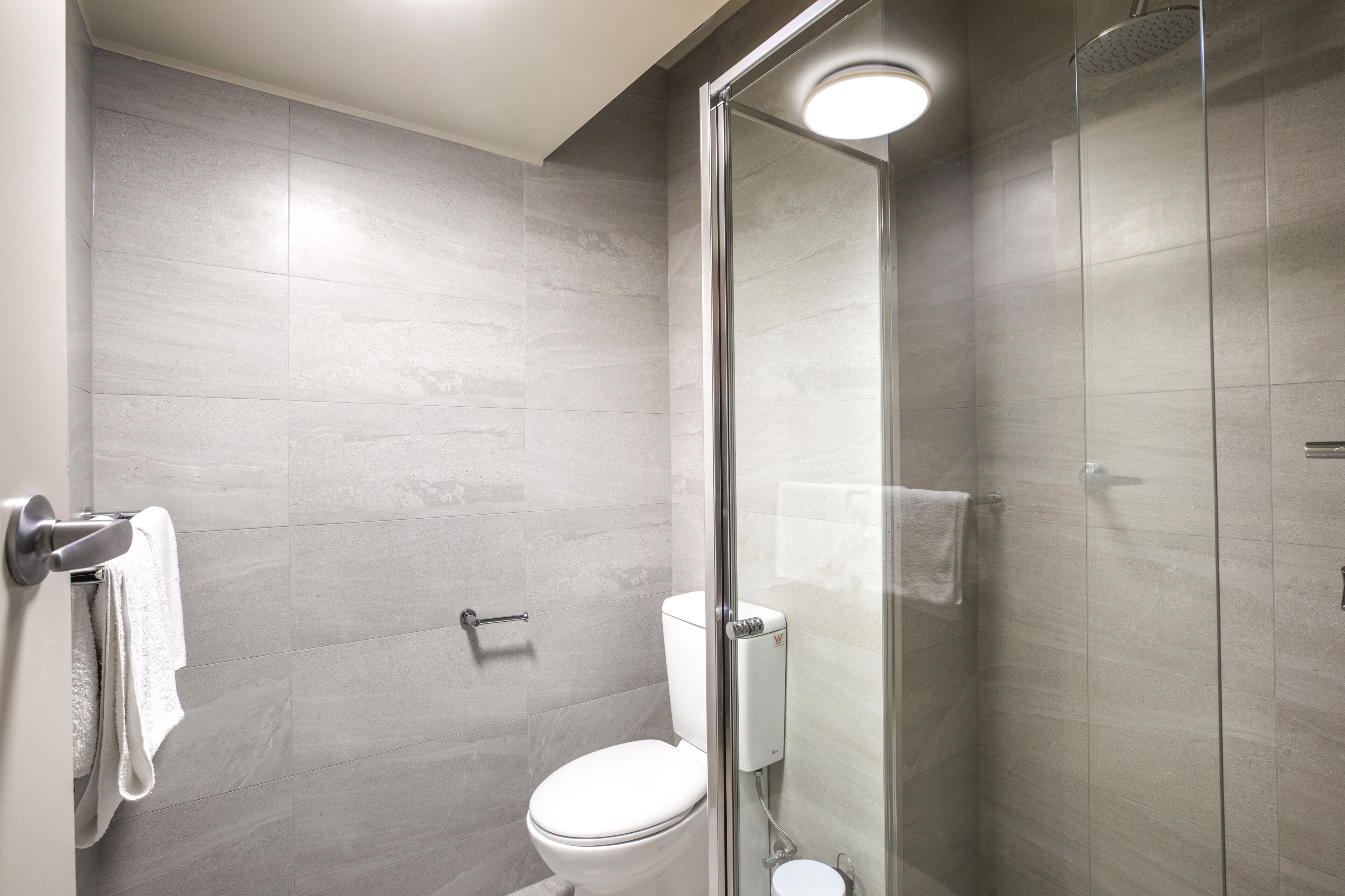 A modern bathroom with a glass-enclosed shower, a toilet, and a towel rack.