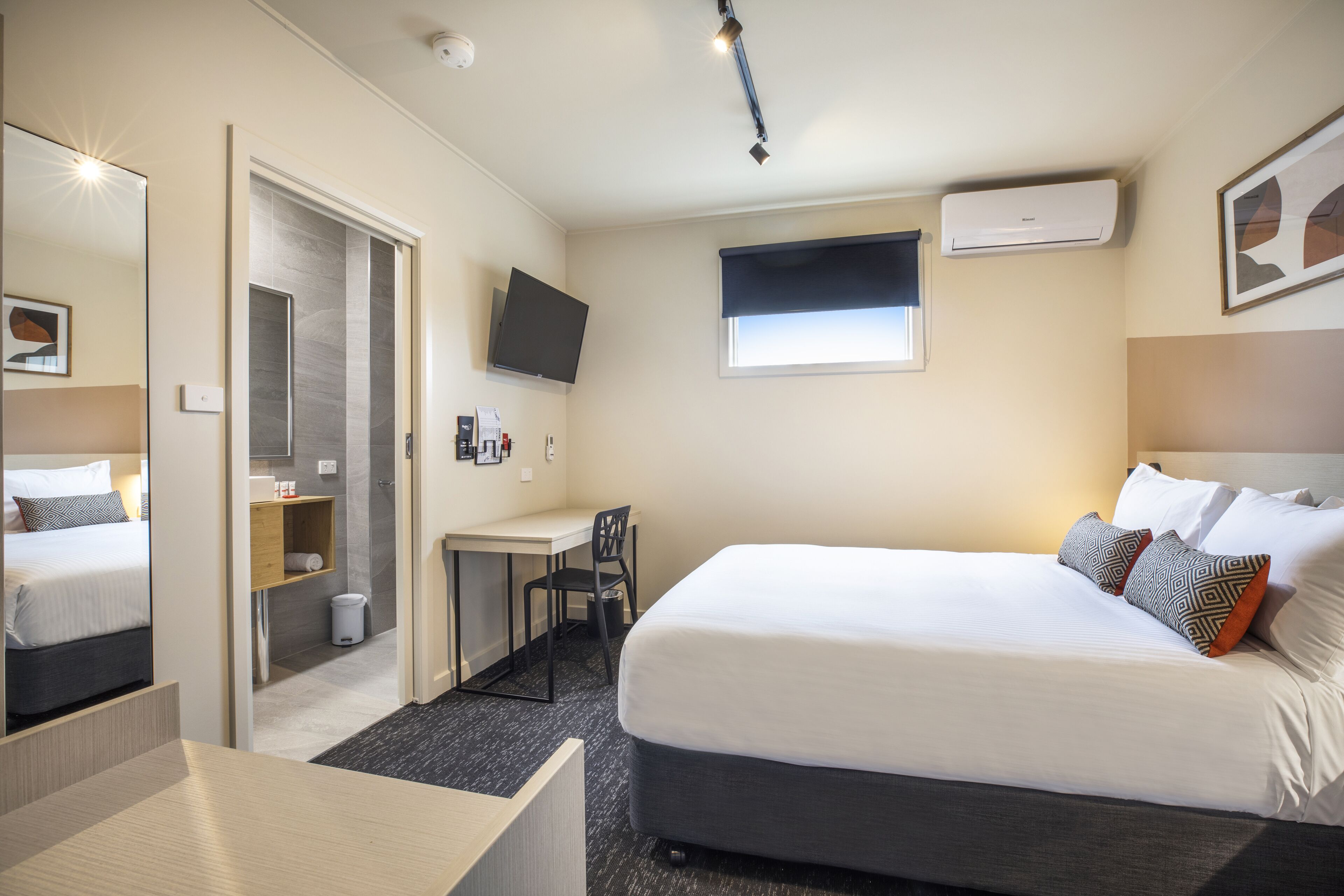 Quarto de hotel com uma cama grande, uma escrivaninha, uma cadeira, uma televisão e uma janela.