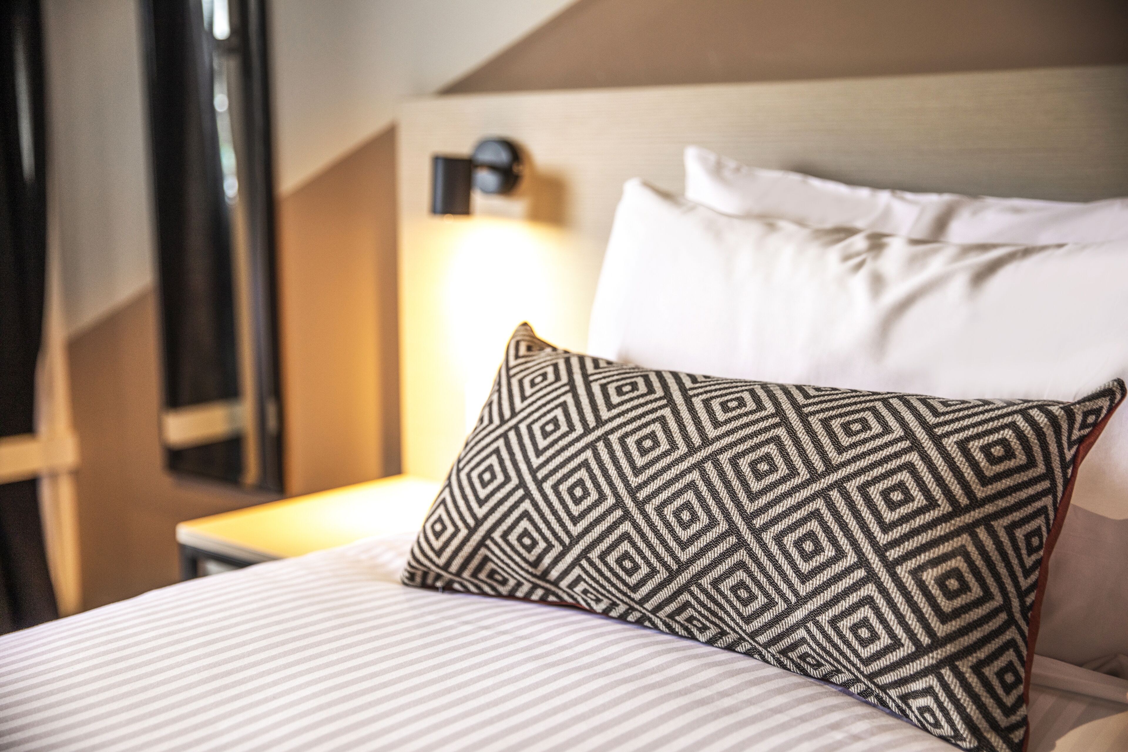 Een net opgemaakt bed met gestreepte kussens en een bedlampje.