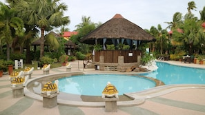 Zona de piscina con una estructura de techo de paja, palmeras y estatuas decorativas de tortugas.