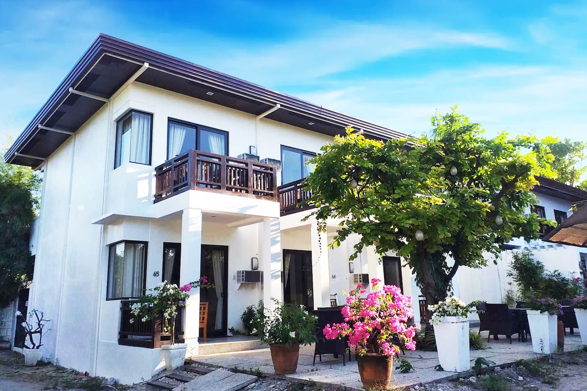 A two-story white building with a balcony, potted plants, and a clear sky.