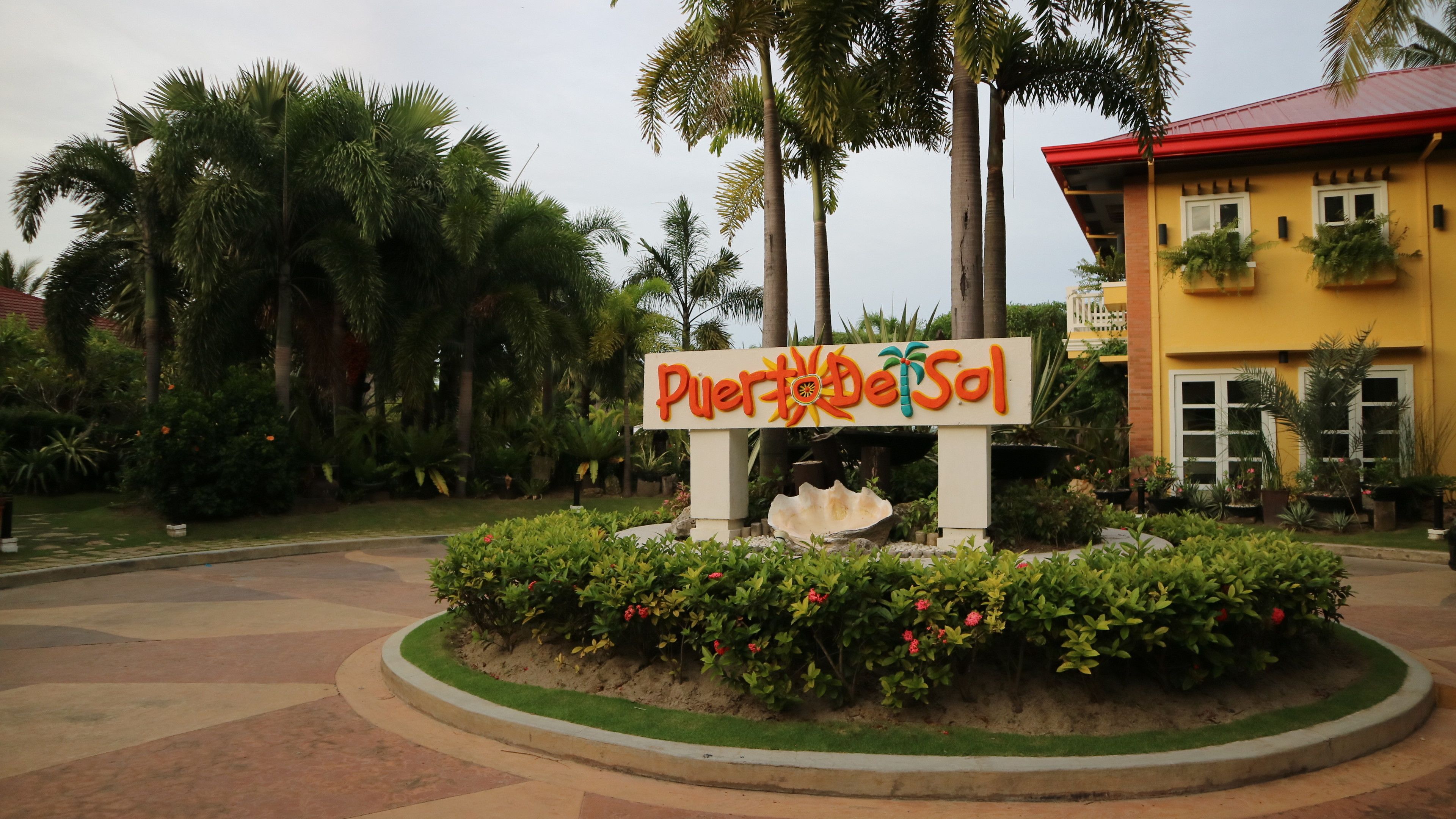 A sign with 'Puerto del Sol' written on it, surrounded by greenery and palm trees.