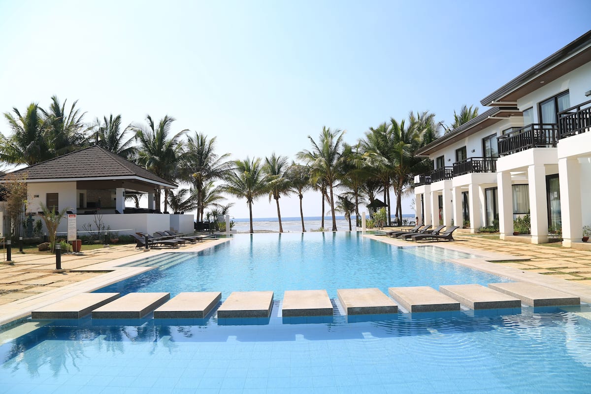 A swimming pool with steps leading into it, surrounded by palm trees and a building with balconies.