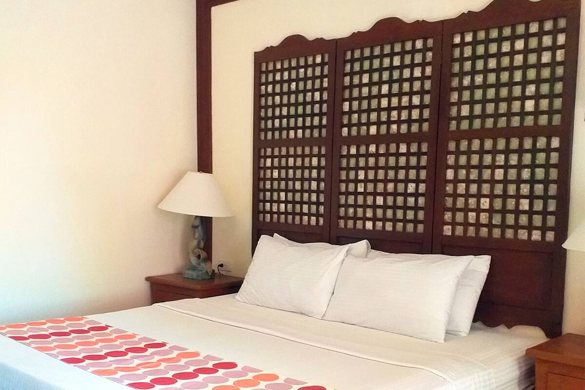 A neatly made bed with a patterned bedspread, a wooden headboard with a lattice design, and a bedside table with a lamp.