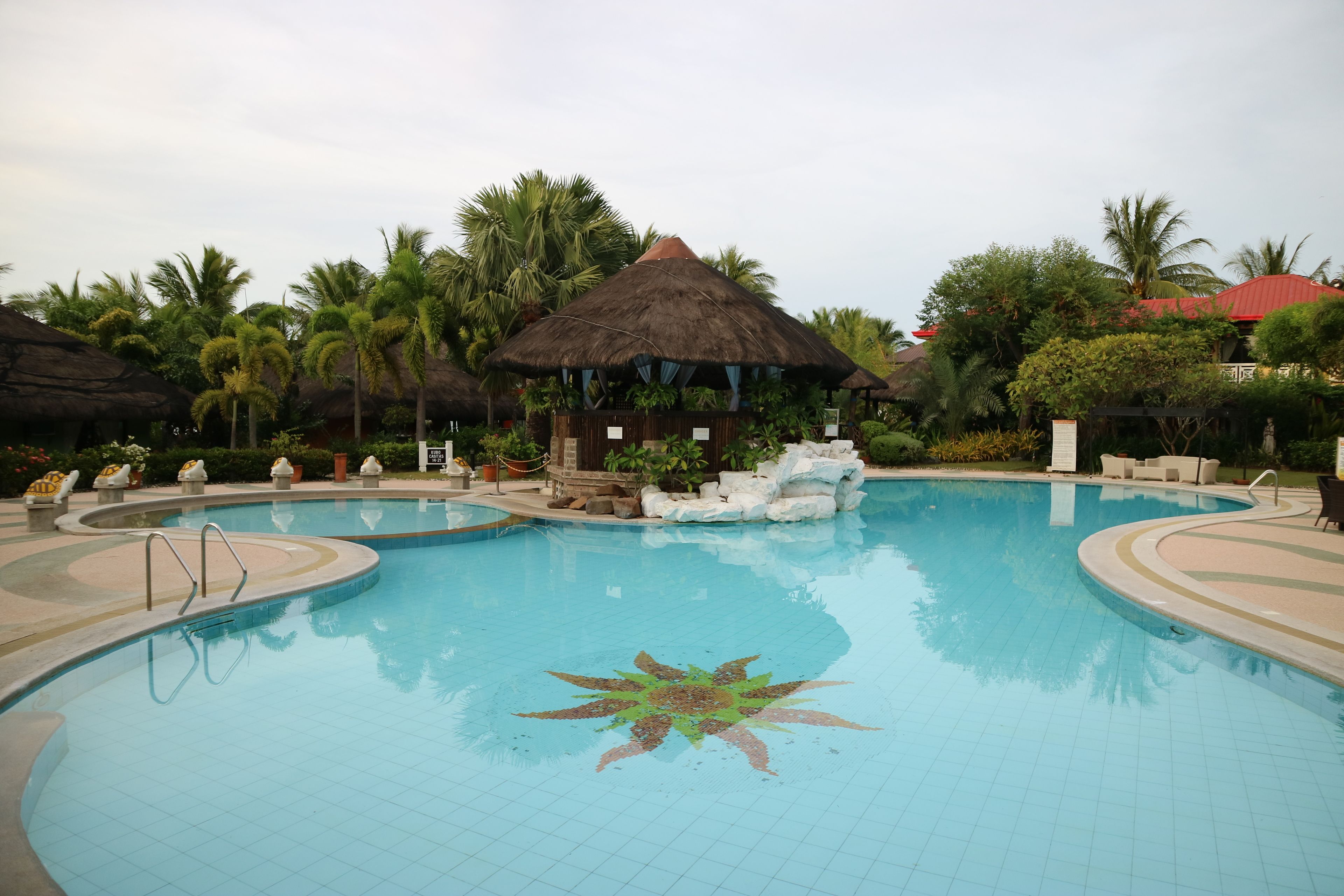 Una piscina con diseño en forma de estrella, rodeada de palmeras y construcciones con techo de paja.