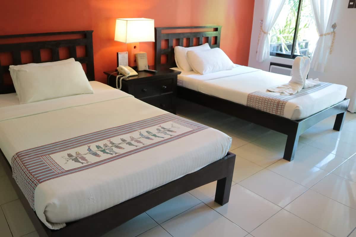 Two single beds with wooden headboards, white bedding, and a small bedside table with a lamp and phone.