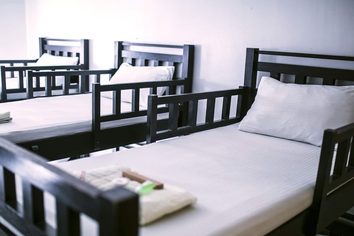 A dormitory room with wooden bunk beds, white bedding, and a small table with a book and a green object.