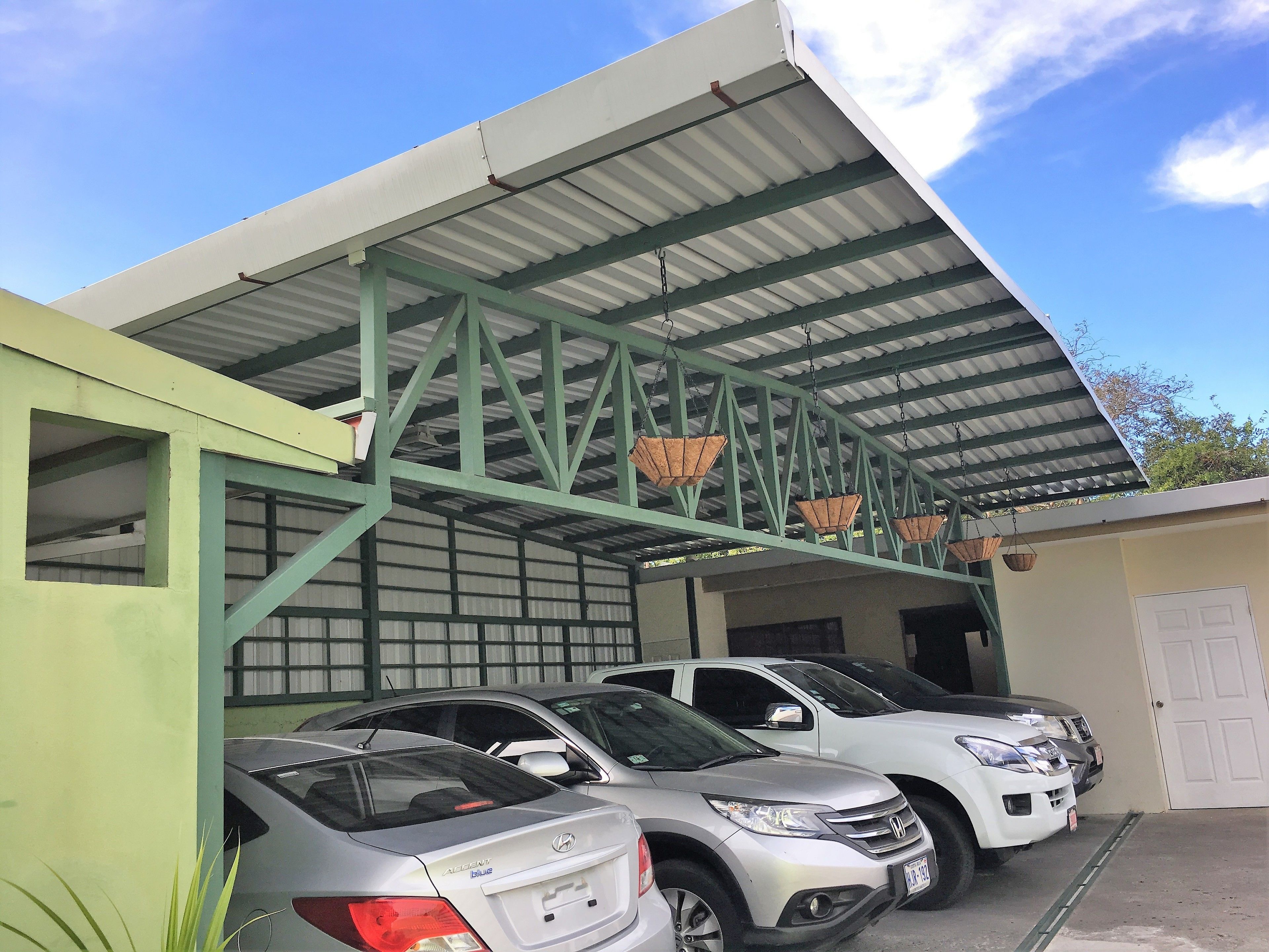 A parking area with several cars, a green metal structure, and hanging baskets.