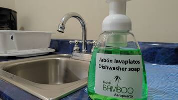 A bathroom sink with a green dish soap bottle labeled "Hotel BAMBOO Aeropuerto."