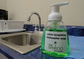 A bathroom sink with a green dish soap bottle labeled "Hotel BAMBOO Aeropuerto."