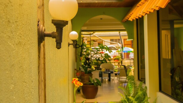 Een gang met een wandlamp, een potplant en uitzicht op een eetgedeelte met tafels en stoelen.
