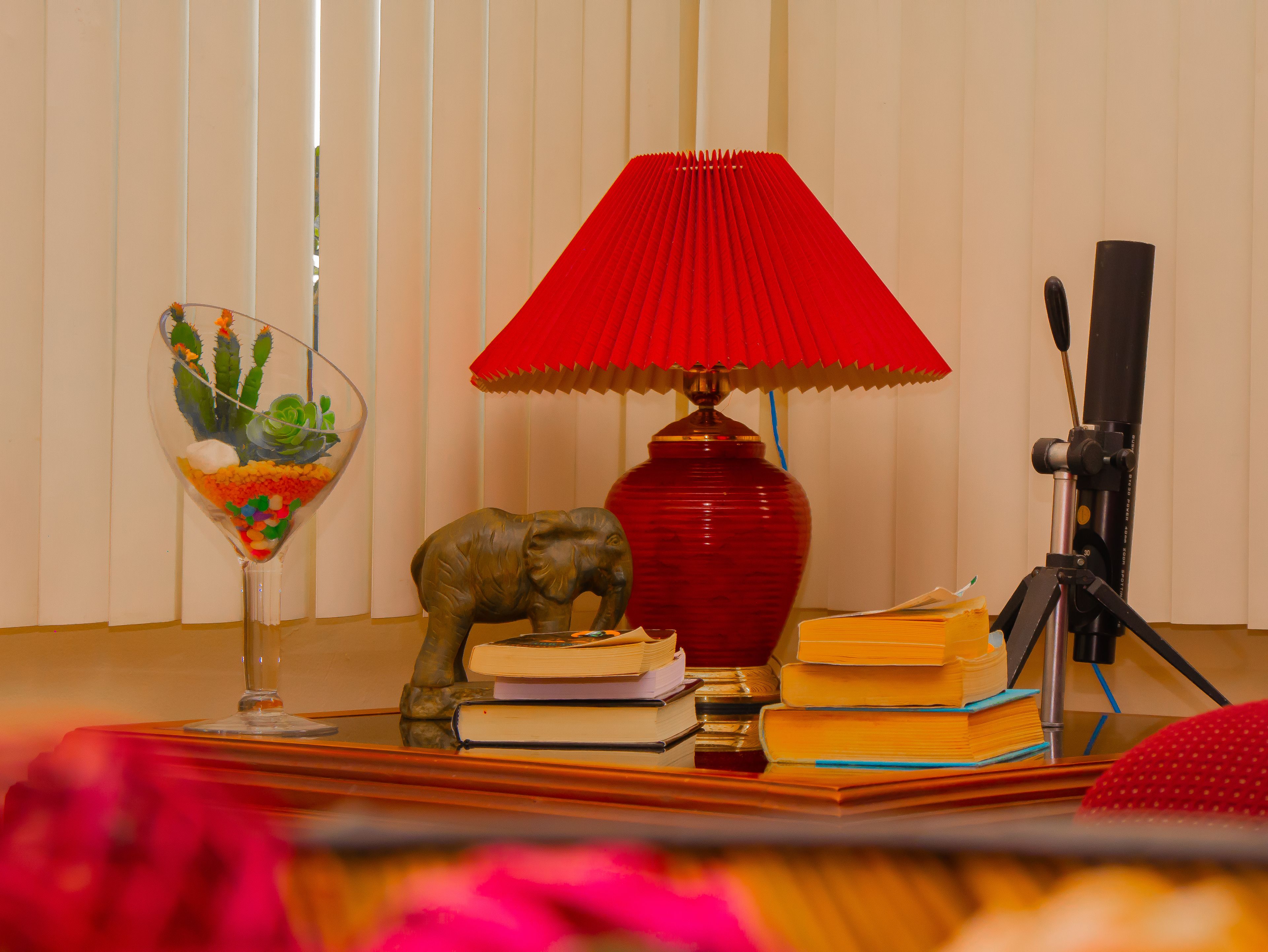 Ein Schreibtisch mit Lampe, Büchern, einer Kamera und einem dekorativen Glas.