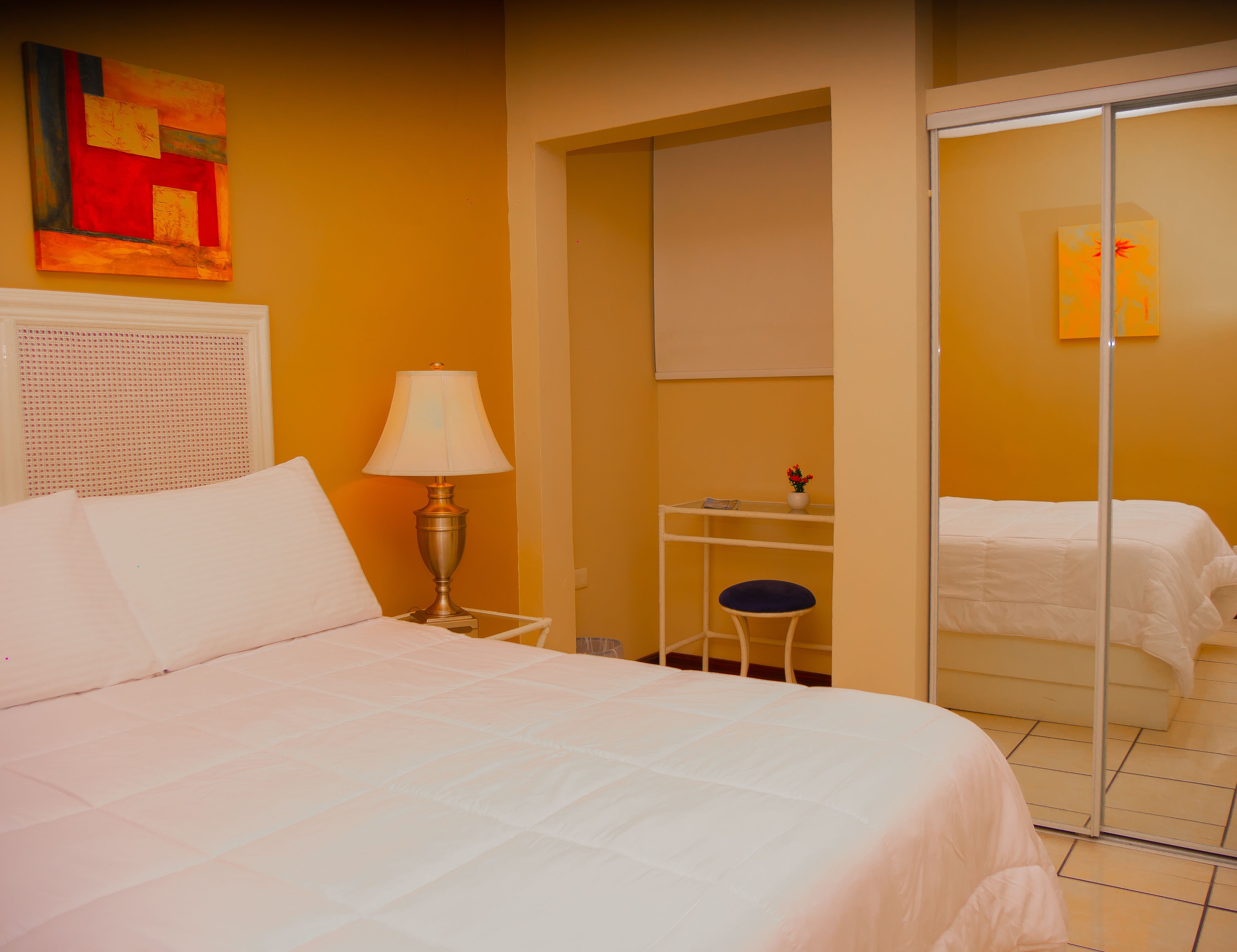 Una habitación de hotel con cama, escritorio, silla, lámpara y espejo.