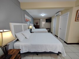 A hotel room with two beds, a bedside table with a lamp, a TV mounted on the wall, and a wardrobe.