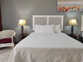 A hotel room with a large bed, two bedside tables with lamps, a white chair, and a painting on the wall.