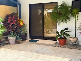 A patio area with potted plants, a sliding glass door, and a tiled floor.
