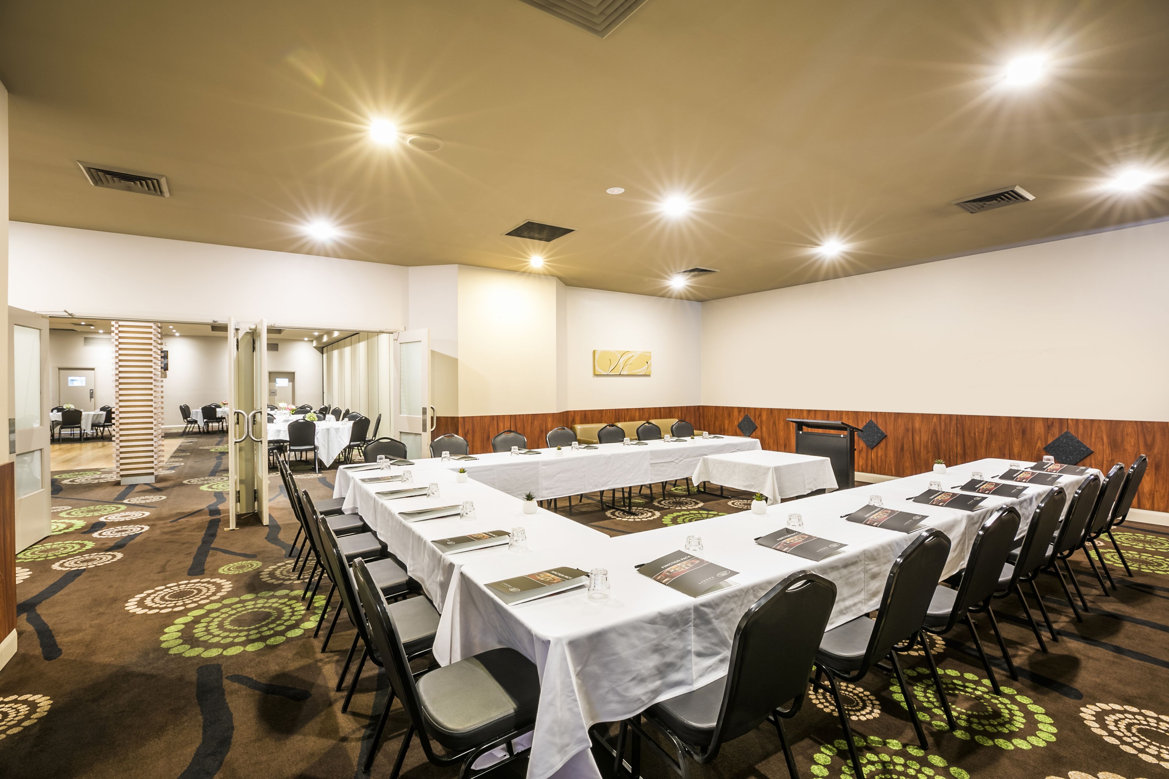 Un salón de conferencias con mesas largas, sillas y piso alfombrado.