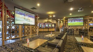 Un hall de hotel con zonas de estar, una recepción y pantallas grandes que muestran eventos deportivos.