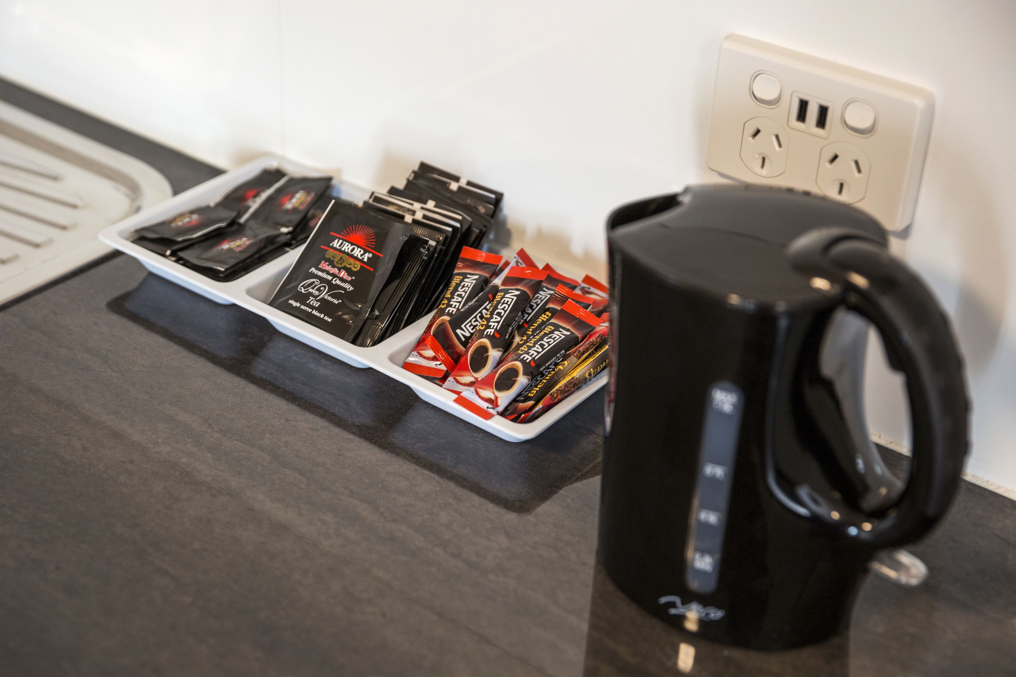 A countertop with a black coffee maker, a tray of coffee pods, and a power outlet.