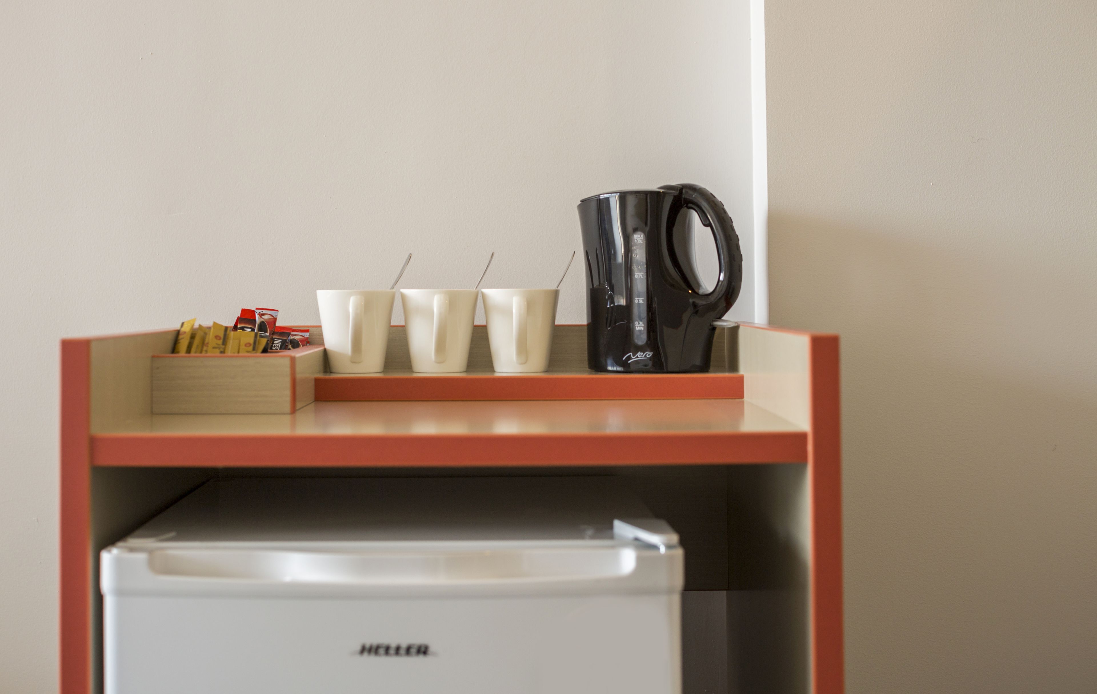 Una kitchenette con cafetera, tazas y refrigerador.