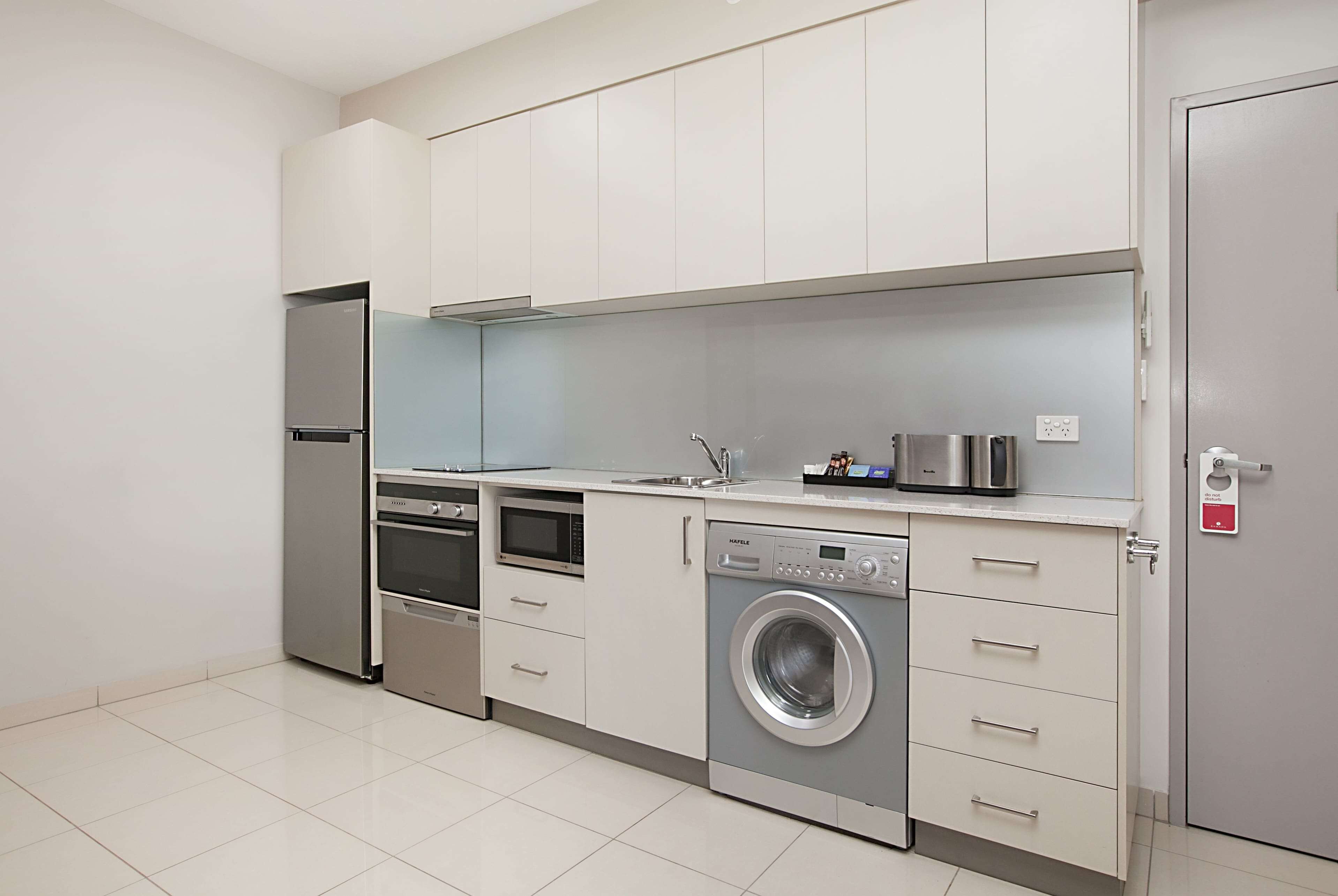 A modern kitchen with stainless steel appliances, a built-in oven, a washing machine, and a microwave.