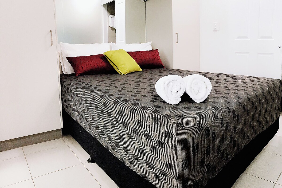 A hotel room with a bed, a mirror, and a pair of rolled towels on the bed.