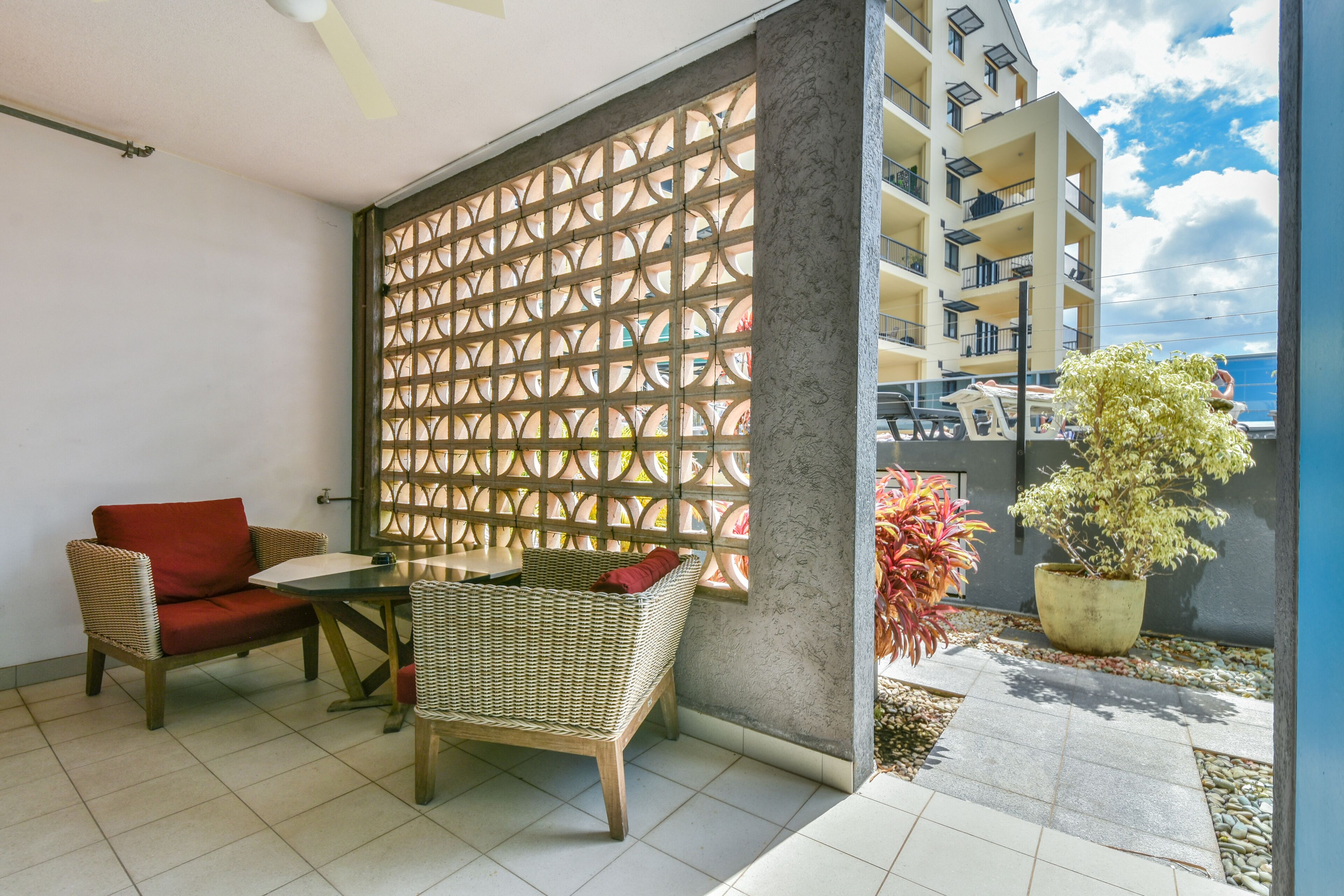 A balcony with wicker furniture, a potted plant, and a view of a building.