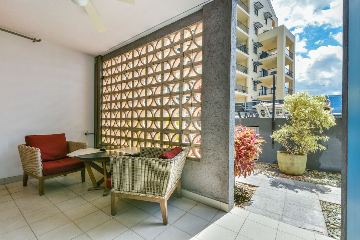 A balcony with wicker furniture, a potted plant, and a view of a building.
