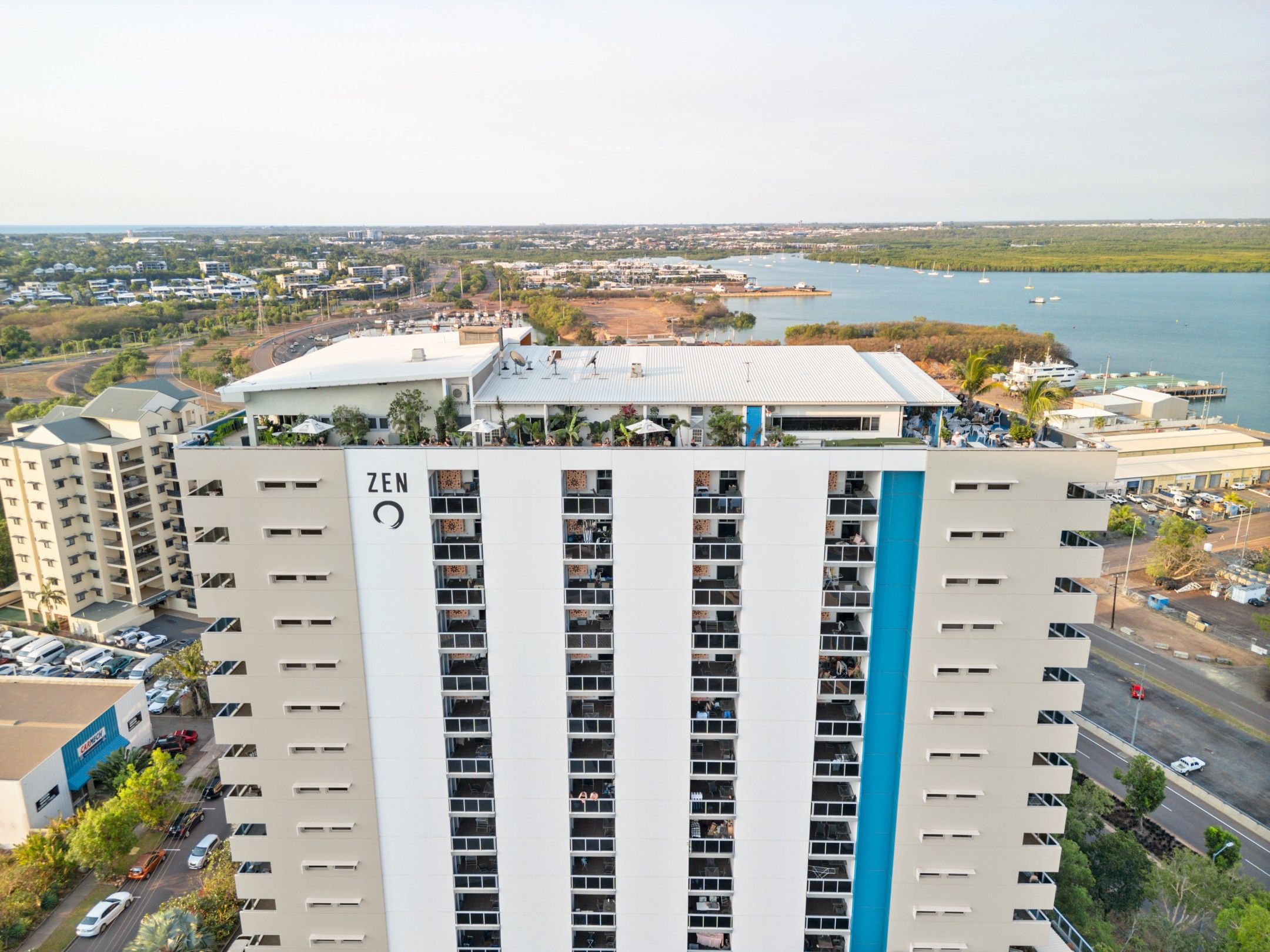 A high-rise building with multiple floors, a prominent 'ZEN' sign, and a view of a marina with boats.