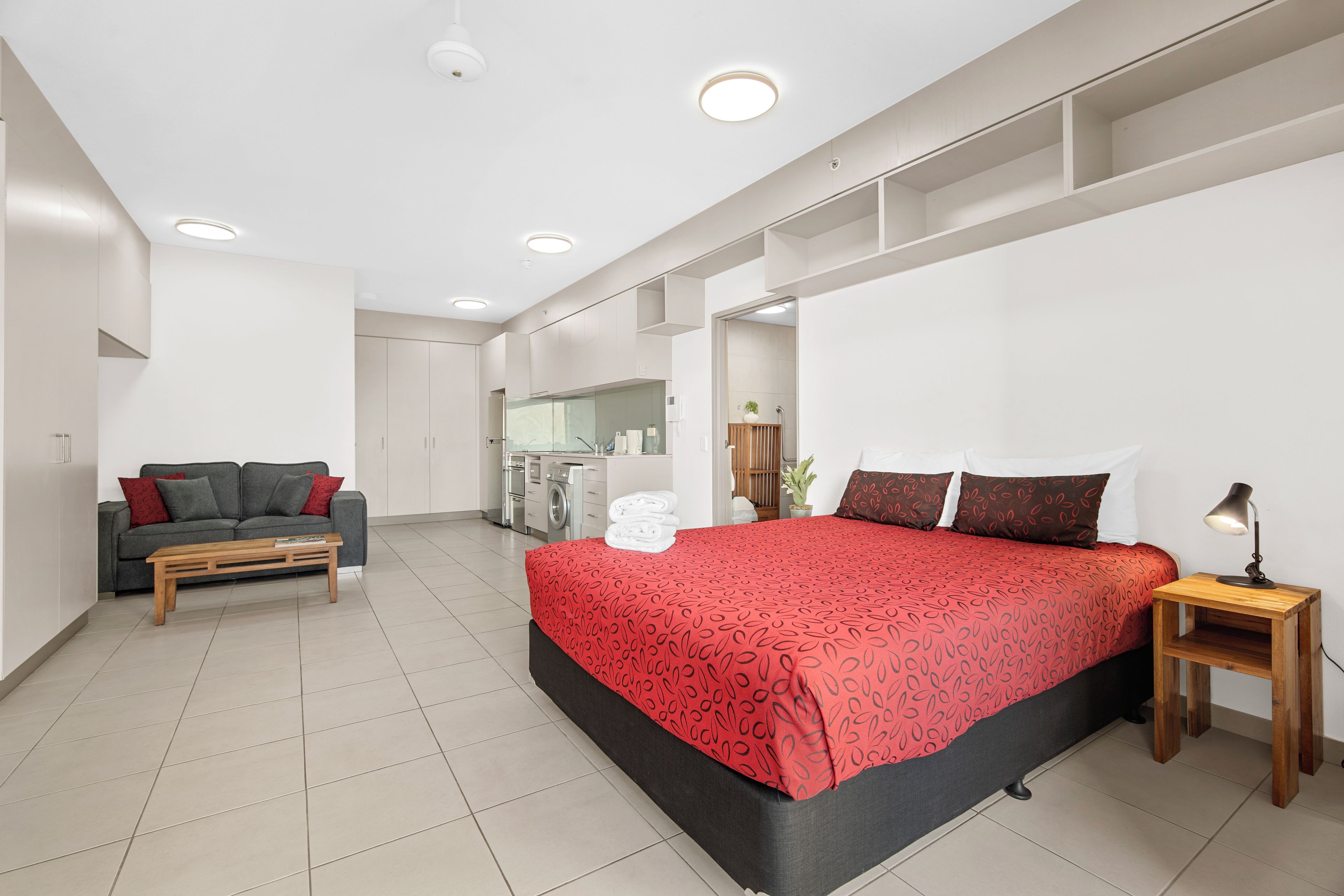 A modern bedroom with a large bed, a sofa, a small table, and a mirror.