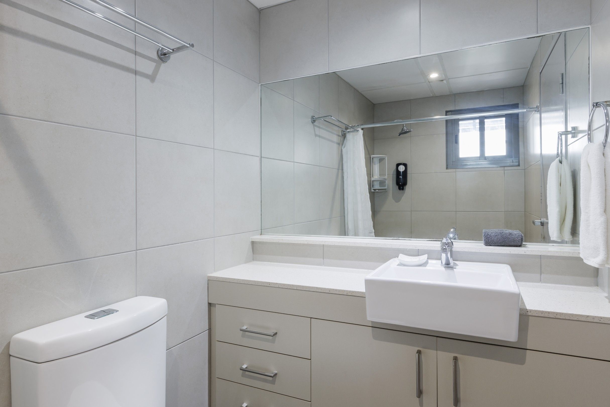 A modern bathroom with a toilet, sink, mirror, and shower area.