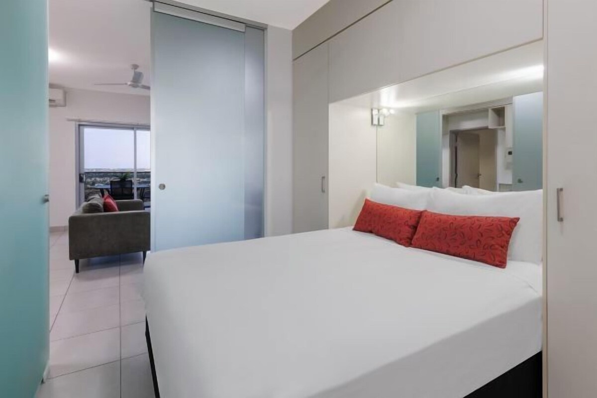 A modern bedroom with a large bed, a wardrobe, and a mirror.