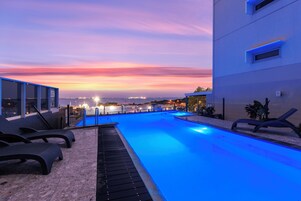 Una piscina en la azotea con sillas de descanso y vistas al atardecer.