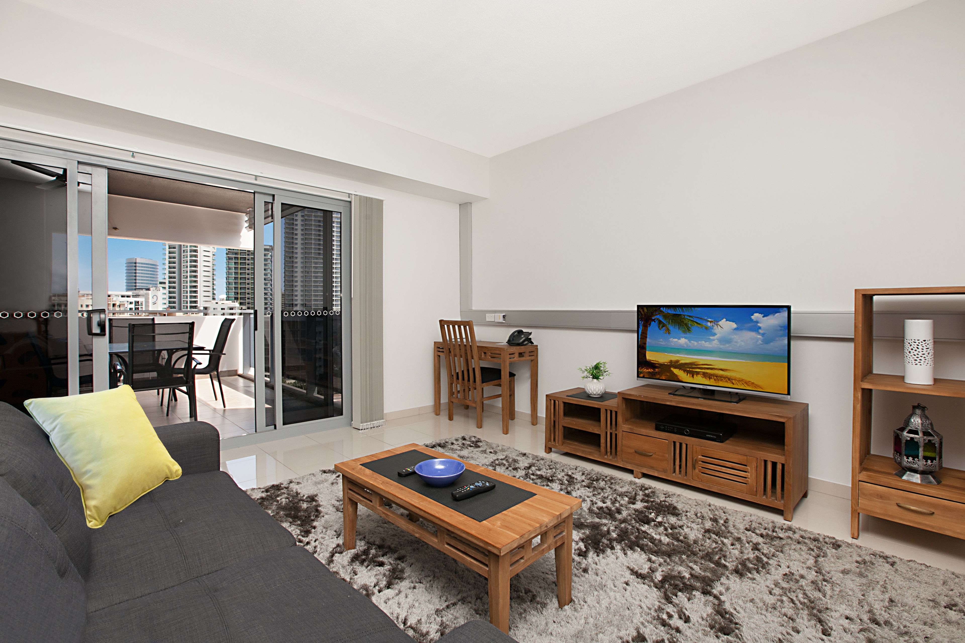 A modern living room with a grey sofa, a wooden coffee table, a TV, and a dining area with chairs and a table.