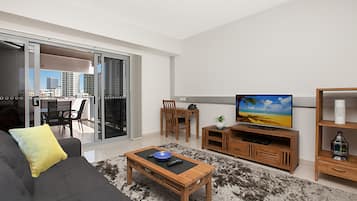 A modern living room with a grey sofa, a wooden coffee table, a TV, and a dining area with chairs and a table.