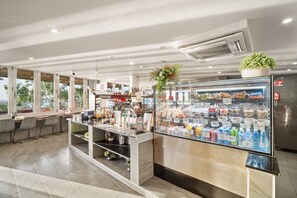 A modern cafe with a self-service counter, a refrigerated display case with snacks, and a seating area with tables and chairs. - Ramada Suites by Wyndham Zen Quarter Darwin (Darwin)