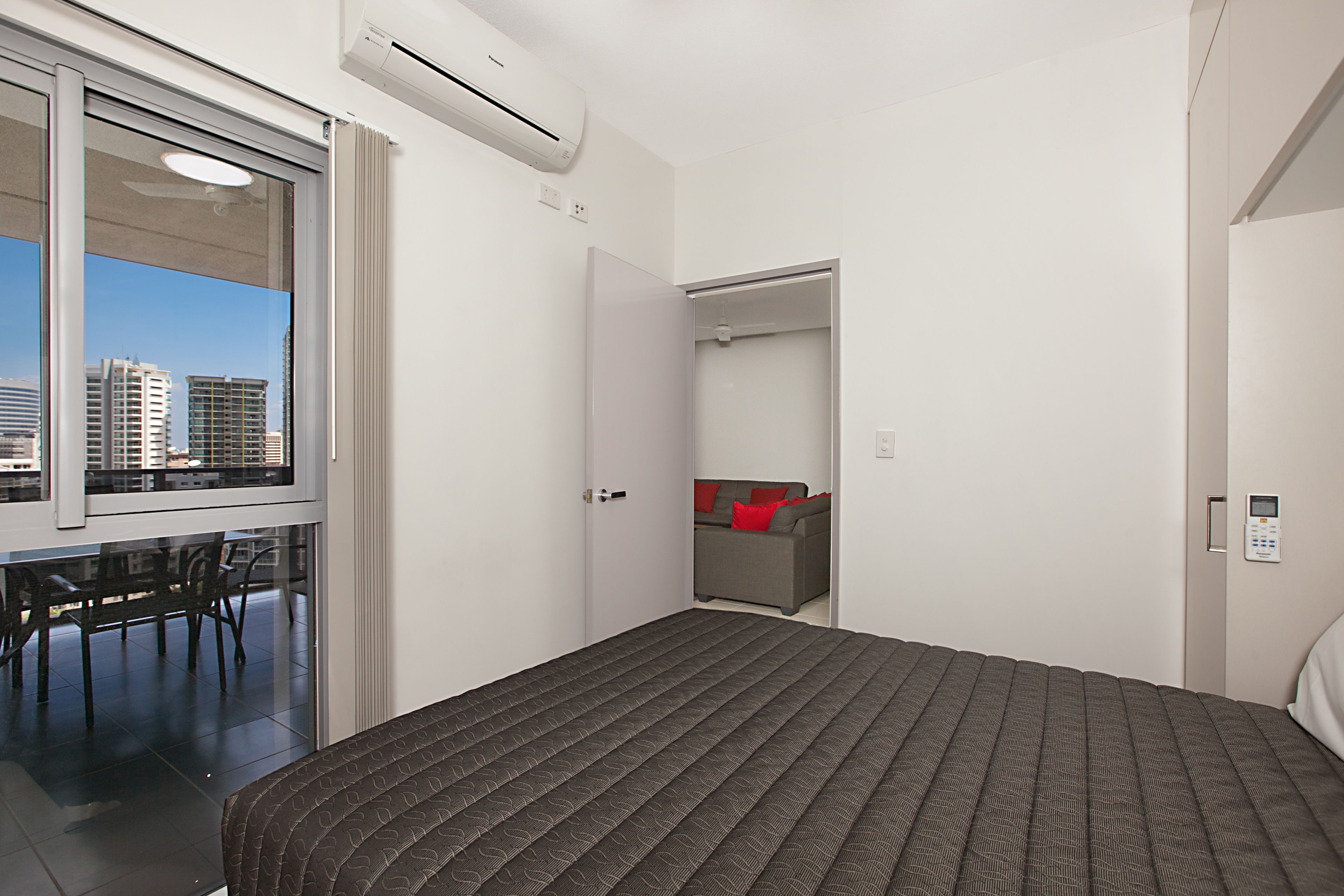 Une chambre d’hôtel moderne dotée d’un grand lit, d’une fenêtre donnant sur la ville, d’une petite table et d’un coin salon avec un canapé et des fauteuils.