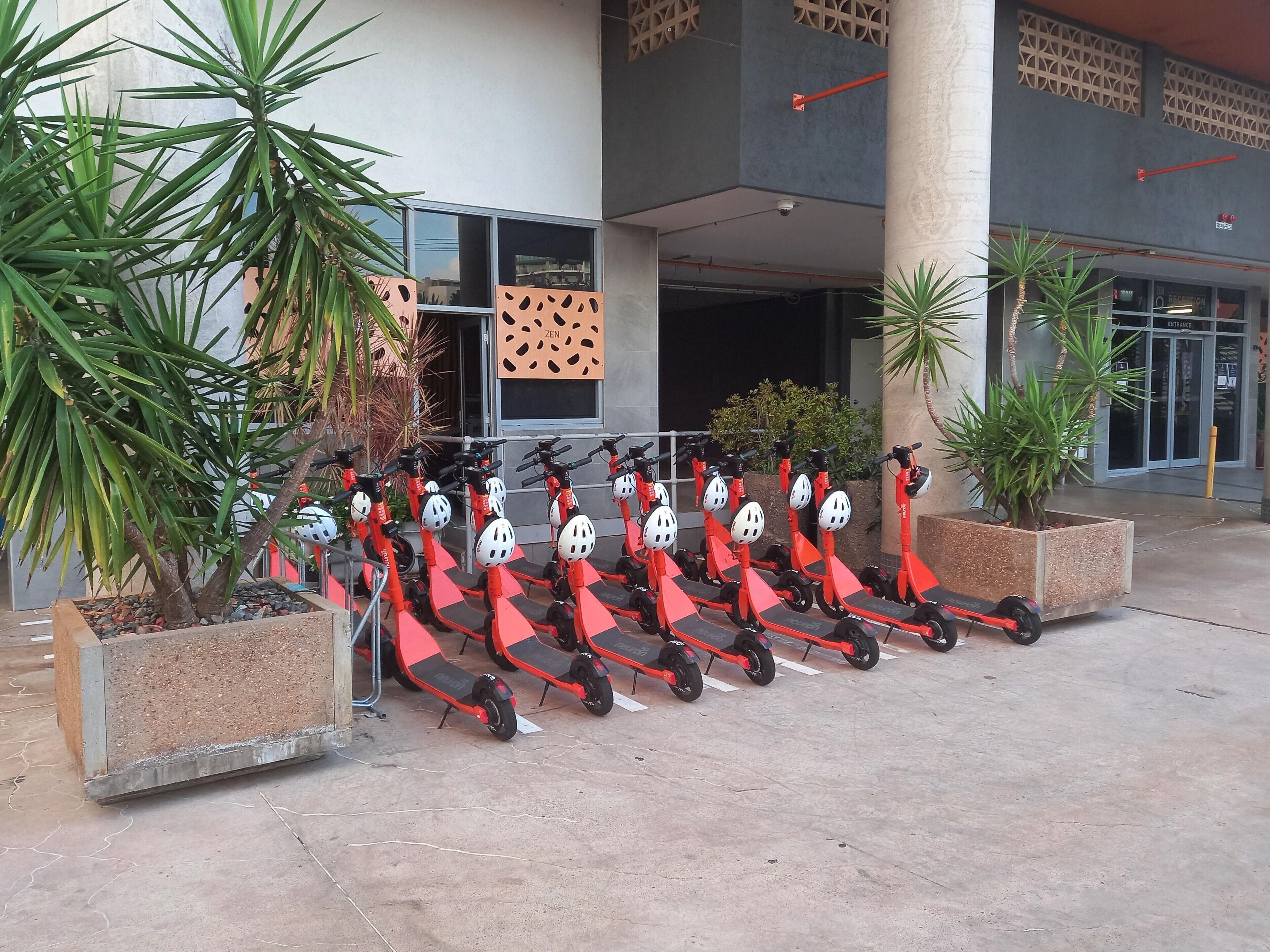 A row of red electric scooters parked in front of a building with a 'Zen' sign.