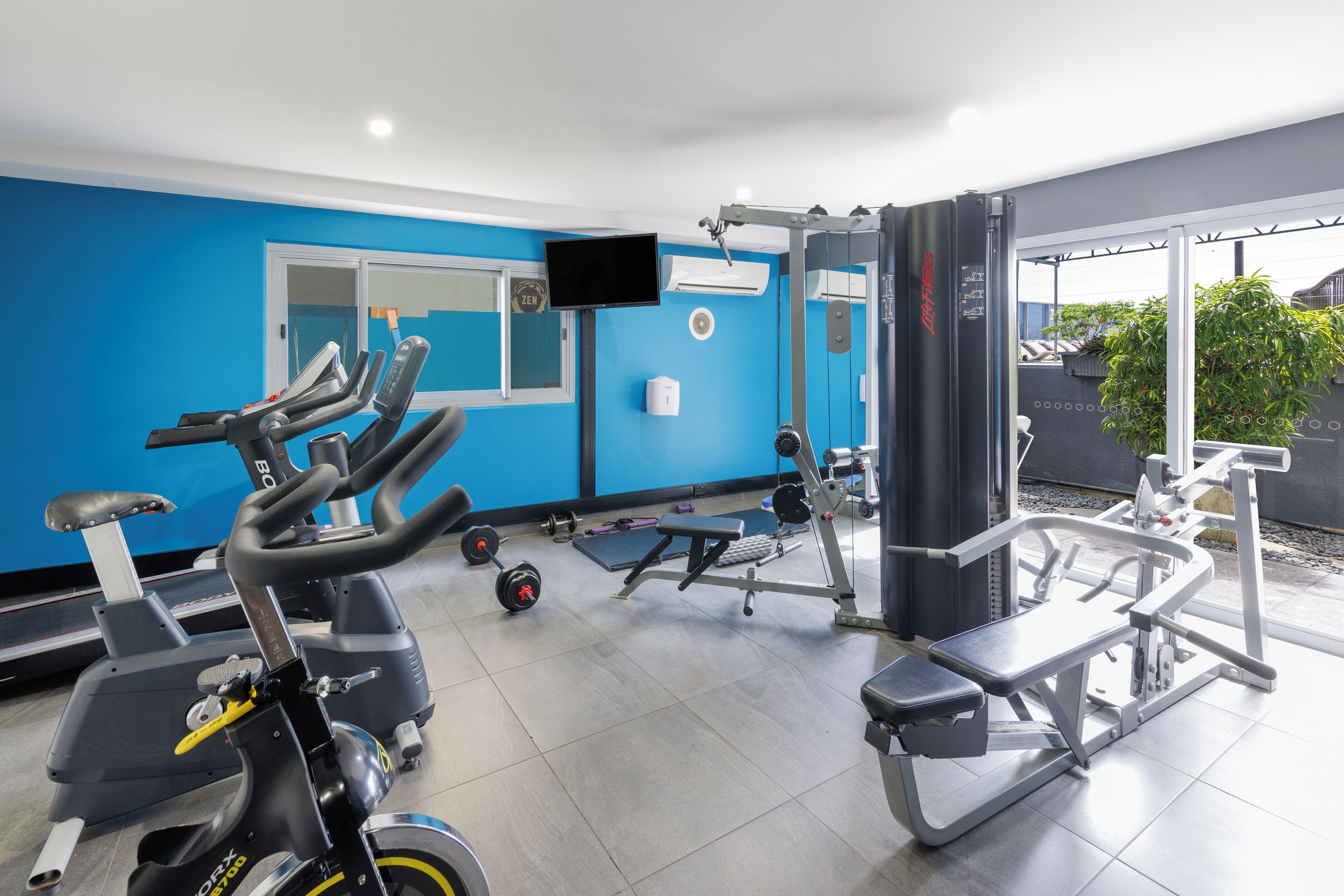 Un gimnasio con equipo de ejercicio, cinta de correr y una pantalla de televisión.