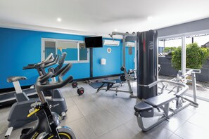 A gym with exercise equipment, a treadmill, and a TV screen. - Ramada Suites by Wyndham Zen Quarter Darwin (Darwin)