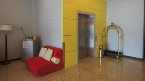 A hotel room with a red sofa, a minibar, an elevator, and a luggage cart. - Princeton Hotel (Johor Bahru)
