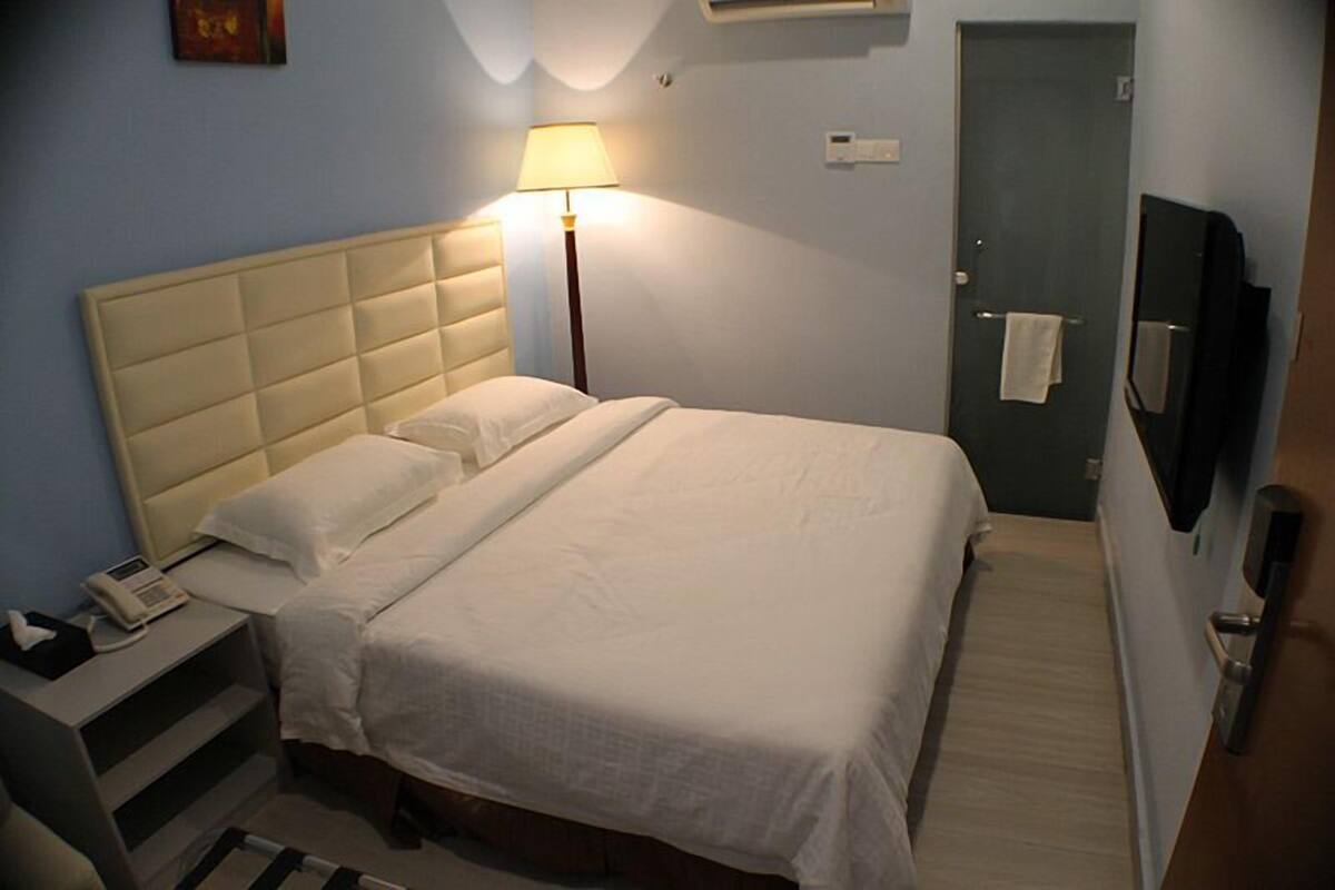 A hotel room with a bed, bedside lamp, bedside phone, and a door with a towel hanging on it.