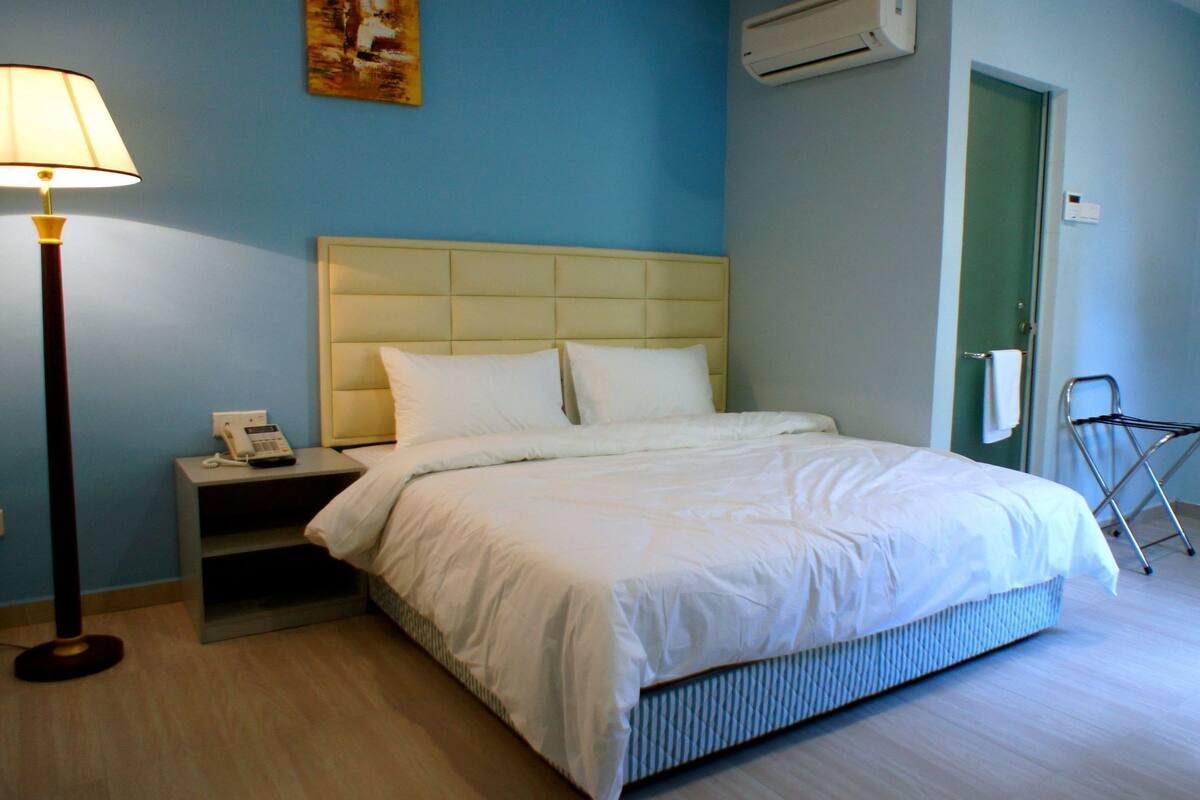 A hotel room with a bed, bedside table, lamp, and a folding chair.