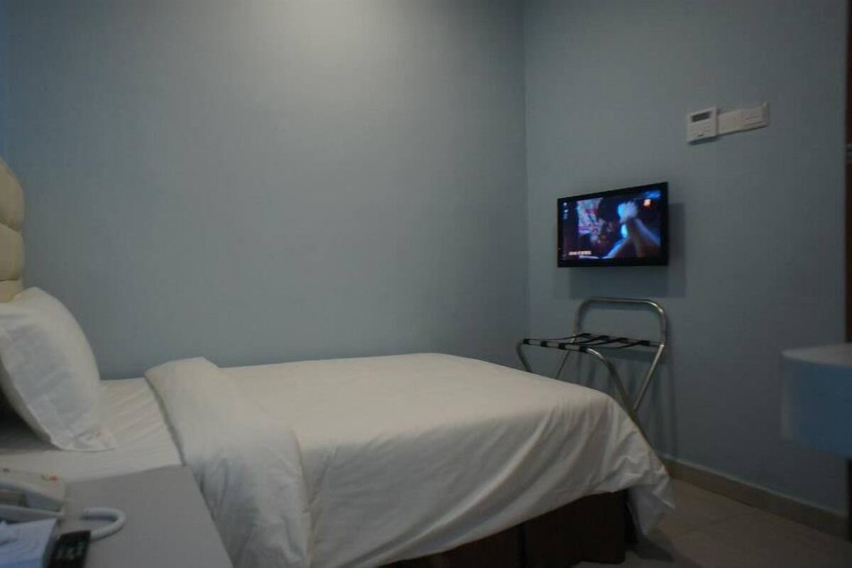 A hotel room with a bed, a chair, a TV on the wall, and a bedside table with a phone.