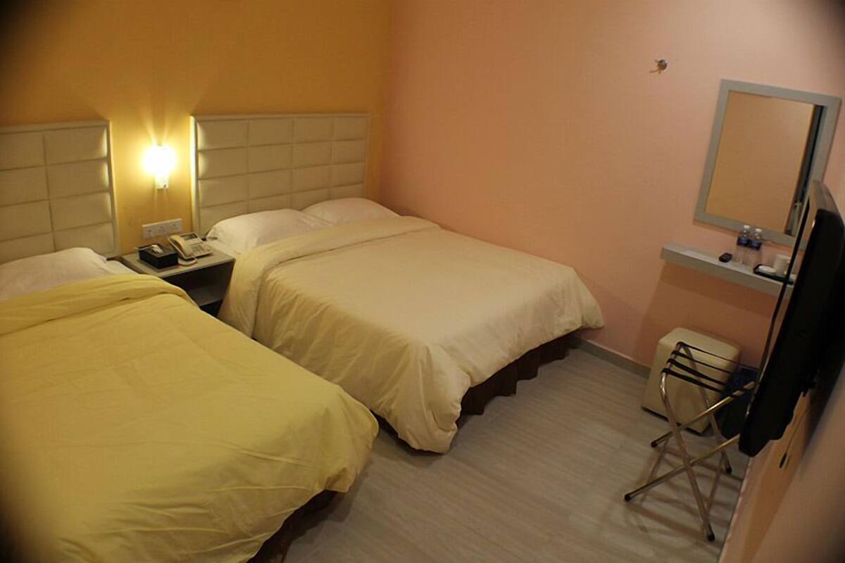 A hotel room with two beds, a bedside table with a lamp, a small desk with a mirror, and a chair.