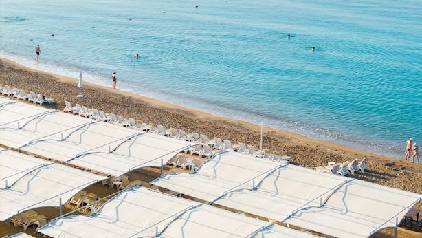 A beach with rows of sunbeds and umbrellas, a sandy shore, and calm blue water. - Corendon Grand Park Lara - Ultra All Inclusive (Antalya)